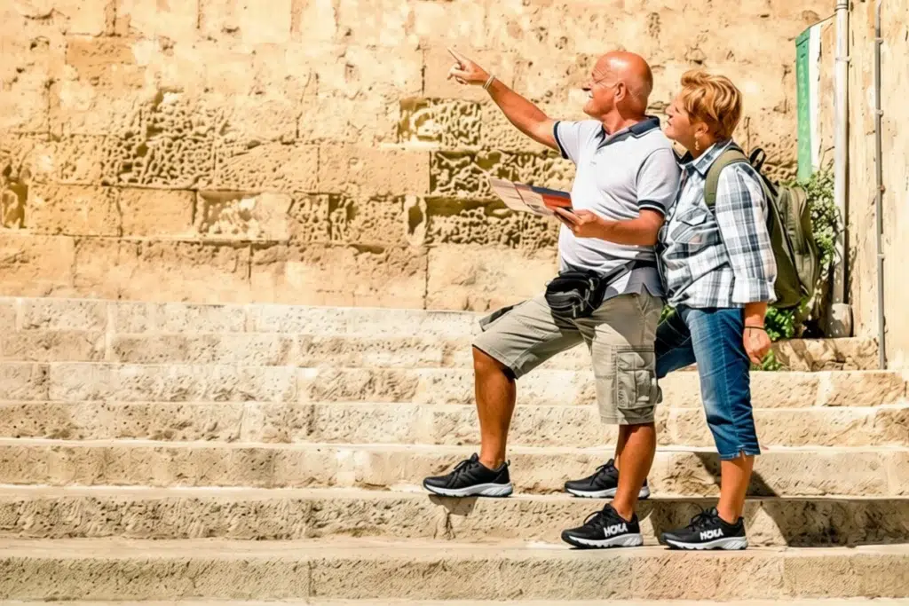 Older couple walking up stone steps wearing supportive athletic shoes, one pointing ahead while holding a map