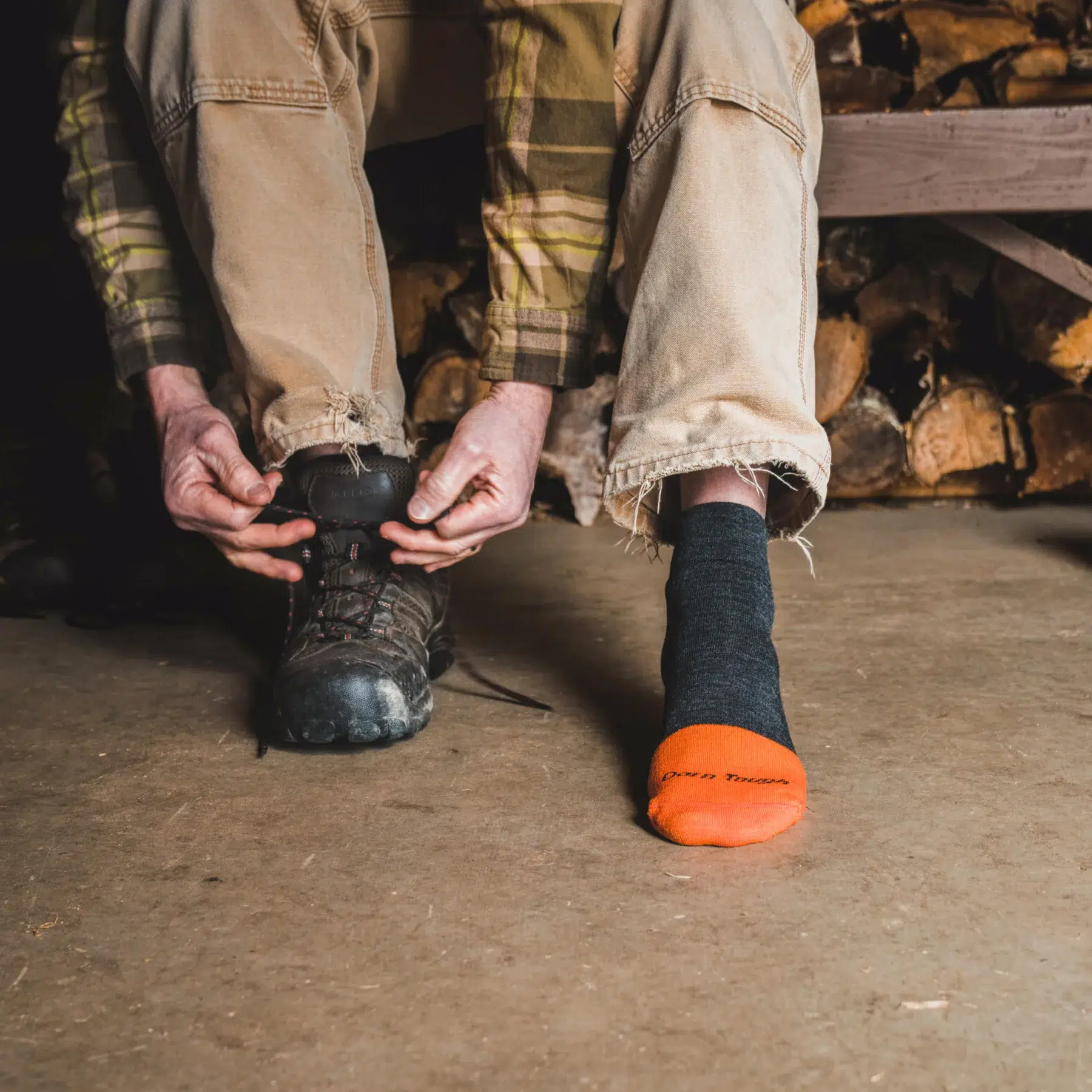 Man tying work boots wearing Darn Tough steely quarter socks indoors
