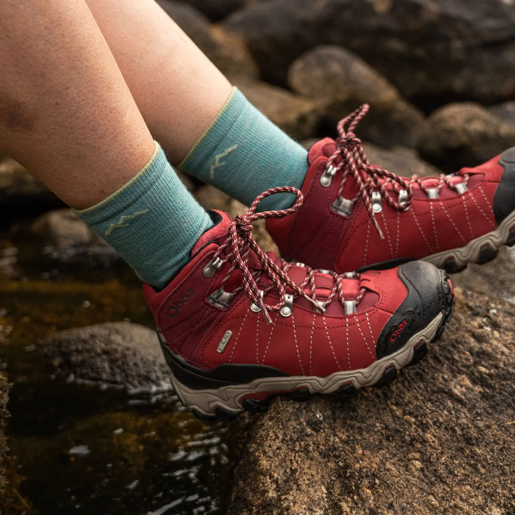 Woman wearing Darn Tough light hike micro crew socks with red hiking boots on rocks