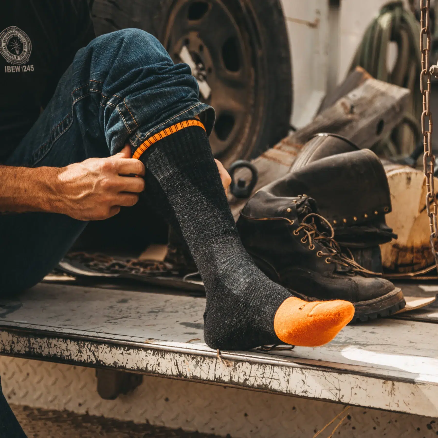 Man putting on work boots wearing Darn Tough steely crew socks in workshop
