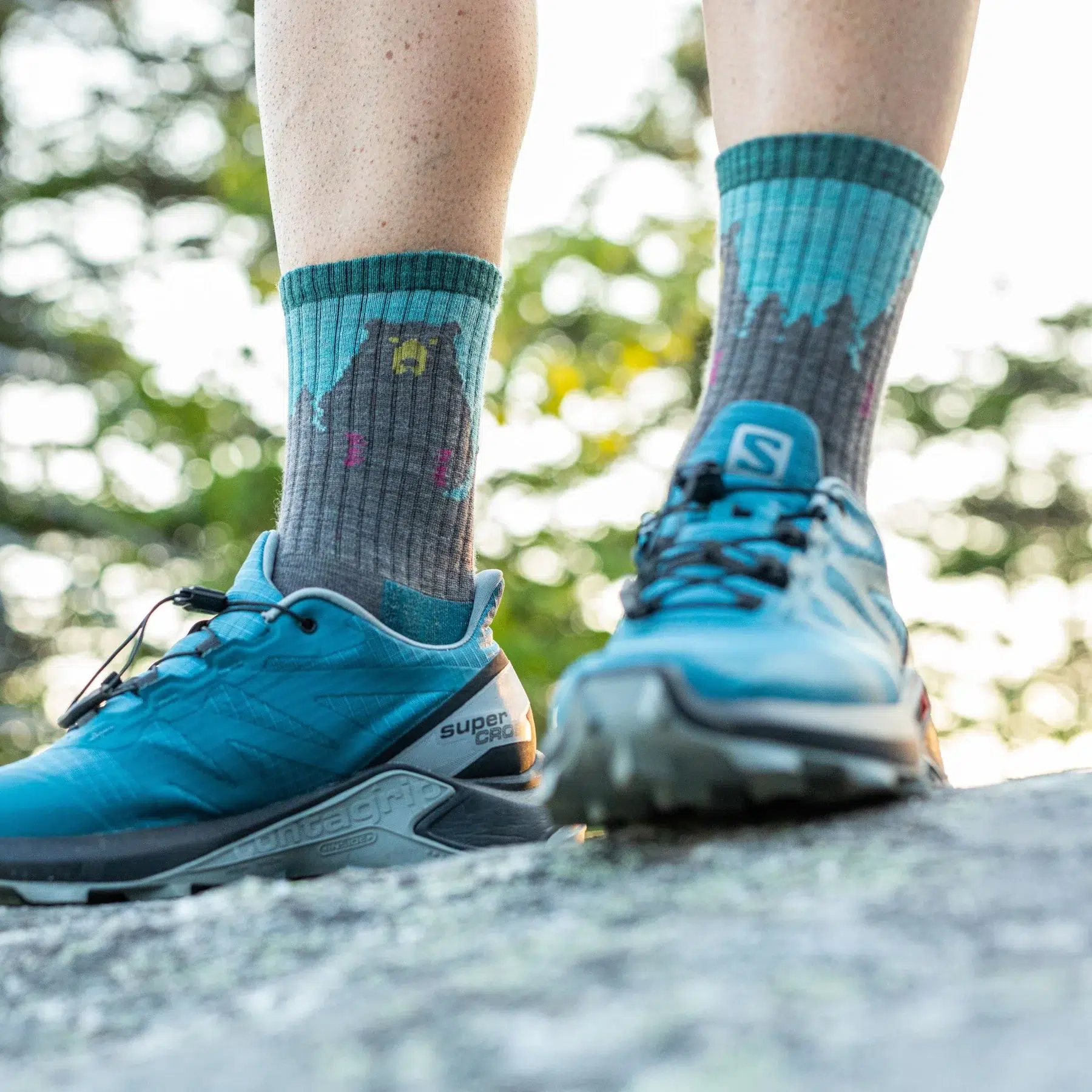 Woman standing on rock wearing Darn Tough light hike micro crew socks with bear pattern and trail shoes