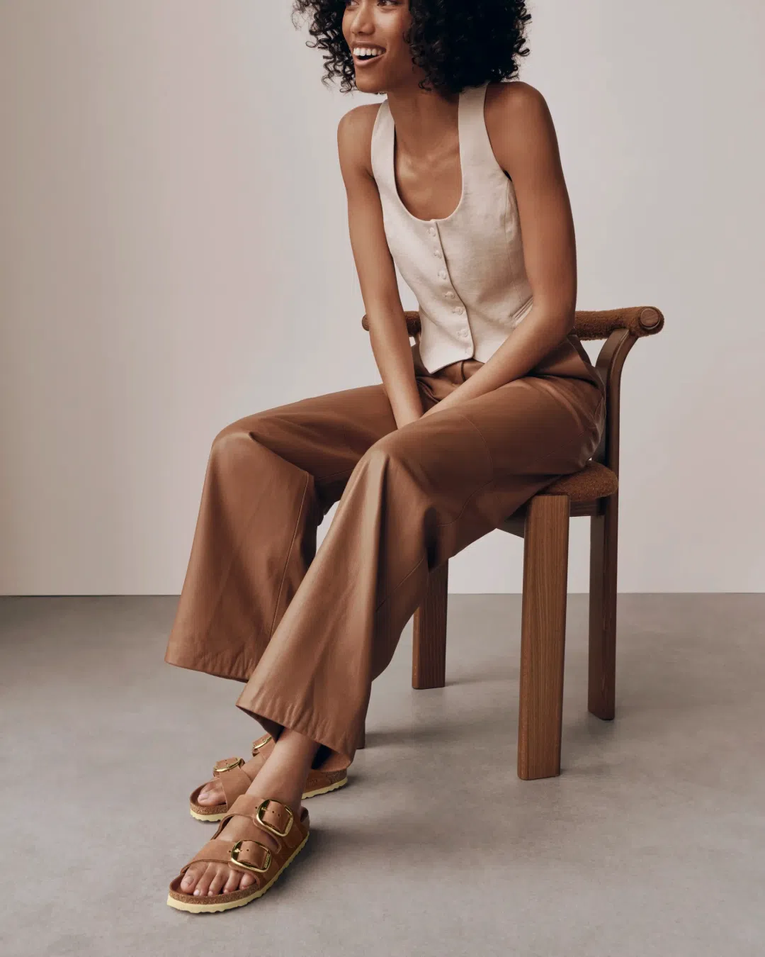 Woman seated on a wooden chair wearing brown Birkenstock Arizona Big Buckle sandals.